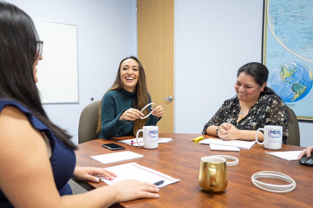 Team members sitting around a table, laughing and discussing a plastic part.